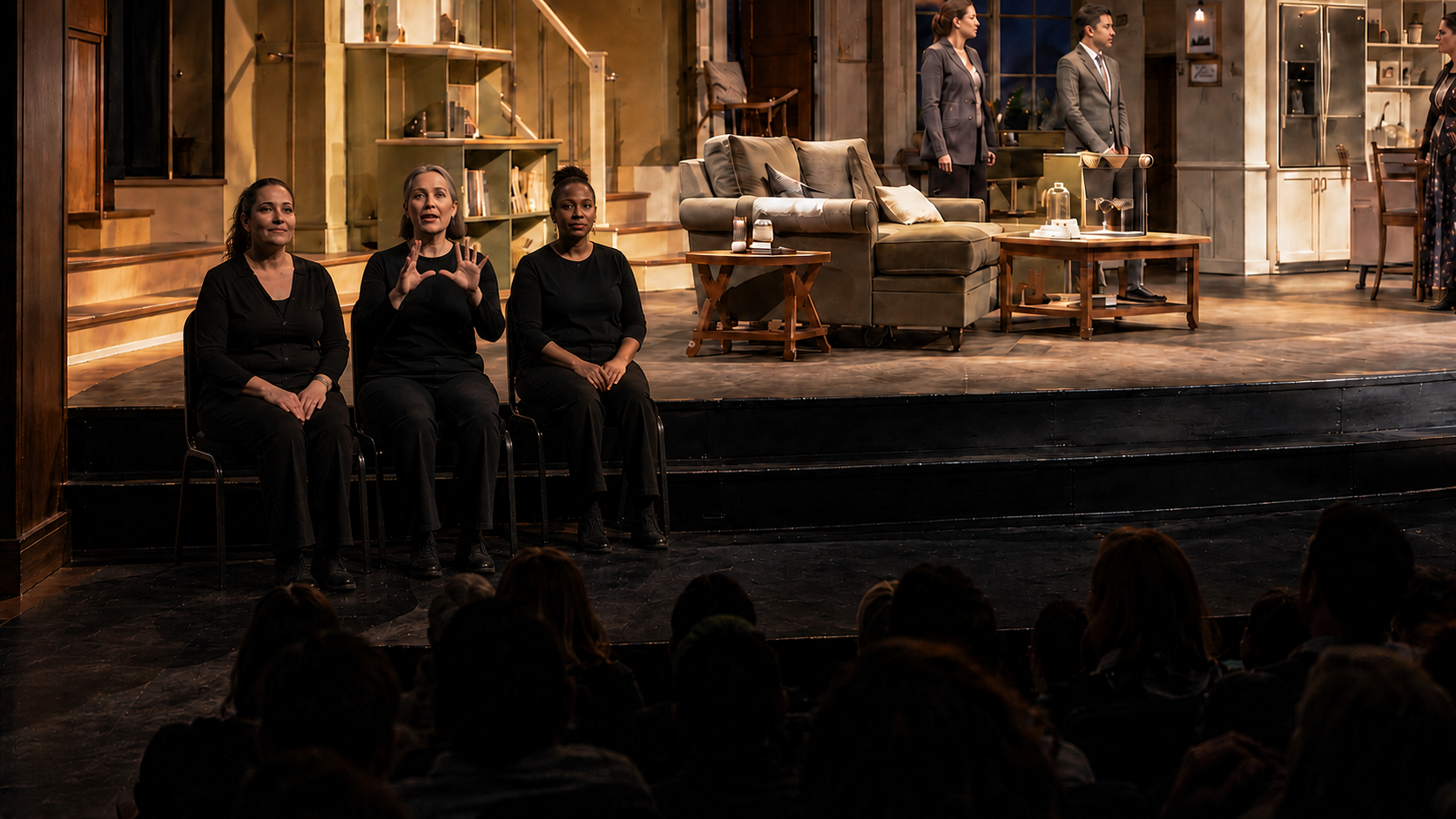 Three seated ASL interpreters and their chairs turned toward the far-left Deaf audience, with the active interpreter facing forward and the play visible directly behind